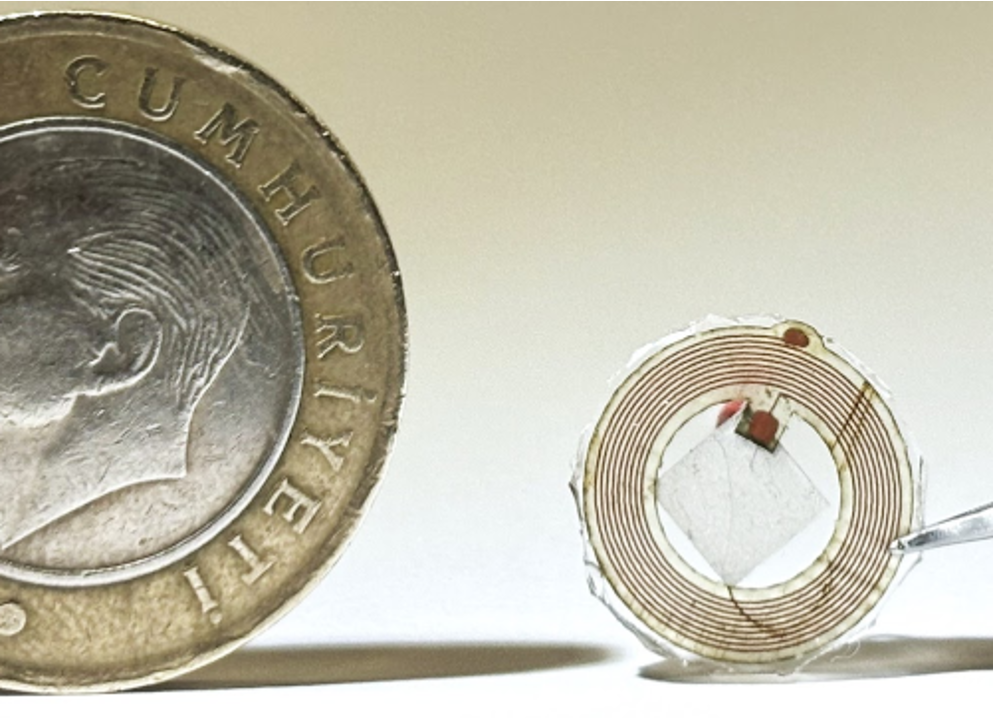Miniature electronics-free wearable ultrasonic tag shown beside a Turkish one-lira coin for scale
